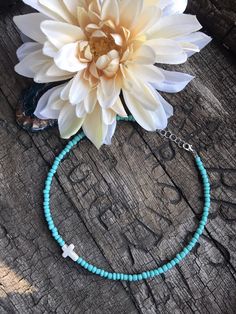 a white flower sitting on top of a wooden table next to a blue beaded bracelet