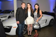 two women and a man standing in front of a white sports car with blue lights behind them