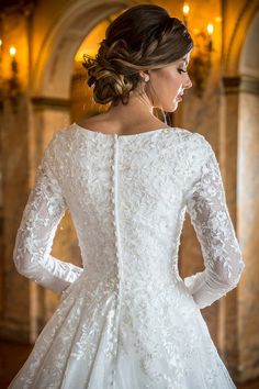 a woman in a white wedding dress looking down at her back with long sleeves on