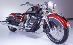 a red and black motorcycle is parked in a white room with its lights turned on