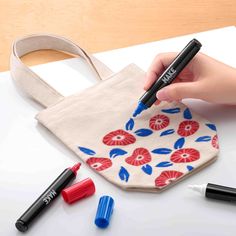 a person is holding a marker in their hand near some markers and a tote bag