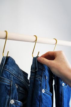 a person holding onto some blue jeans hanging on a white rod with two gold hooks