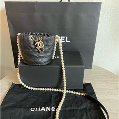 New In The Box This Is An Authentic Chanel Calfskin Quilted Pearl Mini About Pearls Drawstring Bucket Bag In Black. This Crossbody Bag Features A Resin Pearl Shoulder Strap With A Black Leather Shoulder Pad And A Leather Threaded Aged Gold Chain Drawstring. This Opens To A Red Fabric Interior. Base Length: 4.25 In Height: 4.5 In Width: 4.5 In Drop: 23 In Receipt Upon Requested Designer Bucket Bag With Detachable Handle As Gift, Designer Bucket Bag As Gift, Luxury Bucket-shaped Evening Bag For Formal Occasions, Luxury Bucket Evening Bag For Formal Occasions, Luxury Bucket Style Evening Bag For Formal Occasions, Luxury Bucket Style Formal Evening Bag, Designer Leather Bucket Bag As Gift, Luxury Top Handle Bucket Bag For Gift, Luxury Bucket Bag With Removable Pouch For Gifts