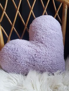 a purple pillow sitting on top of a white fur covered chair next to a black wall