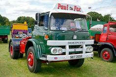 an old green truck parked on top of a grass covered field next to other trucks