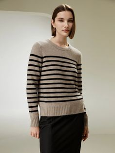 a woman standing in front of a white wall wearing a black and grey striped sweater