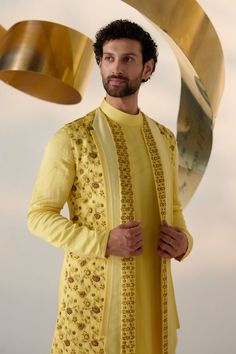 Summer Love Shrug Set | Jatin Malik Introducing our vibrant lemon yellow shrug set, adorned with intricate floral hand embroidery and three types of embroidered lapels in shades of yellow. This ensemble radiates freshness and sophistication, capturing attention with its intricate detailing and vibrant color palette. Paired with an embroidered shoulder-button kurta and tapered trousers, this outfit offers a perfect balance of elegance and contemporary style. Ideal for special occasions, this ensemble is sure to make a statement with its unique design and impeccable craftsmanship. Included in purchase: Shrug Set, Kurta, Trousers Product Specification Color: Yellow Fabric: Linen Silk Occasion: Engagement, Wedding, Bridal, Reception Style: Shrug Set, Kurta, Trousers Care: Dry Clean Work: Hand Designer Yellow Sherwani For Eid, Transitional Designer Wear Yellow Sherwani, Yellow Designer Sherwani With Traditional Drape, Yellow Sherwani With Traditional Drape, Yellow Kurta For Diwali Reception, Elegant Yellow Designer Wear Sets, Elegant Yellow Sets With Resham Embroidery, Yellow Embroidered Kurta For Reception, Traditional Yellow Sherwani For Designer Wear