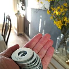 a person holding a stack of metal discs in their hand next to a vase with yellow flowers