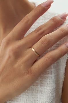 a woman's hand with a gold ring on her left wrist, wearing a white dress