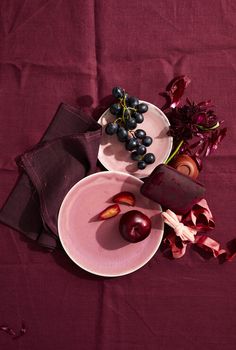 two plates with fruit on them are sitting on a purple table cloth next to flowers