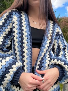 a woman wearing a blue and white crochet jacket with her hands in her pockets