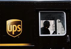 the ups logo is on the side of a black truck with gold lettering and a man looking out the window