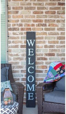 a welcome sign sitting on the side of a brick wall next to two wicker chairs