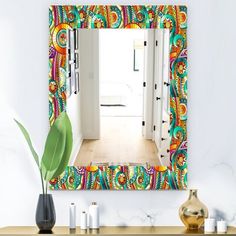 a colorful mirror hanging on the side of a wall next to a vase and plant