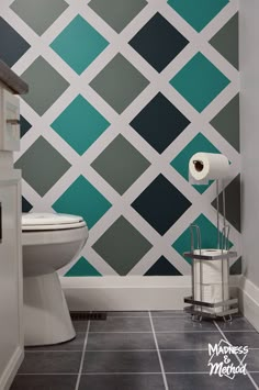 a bathroom with a toilet, sink and wallpaper in blue and green squares on the walls