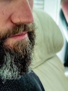 a close up of a man with a beard and piercing on his nose looking at the camera