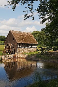 an old water mill sits in the middle of a field next to a pond and trees