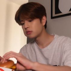 a young man sitting at a table with a hot dog in front of his face