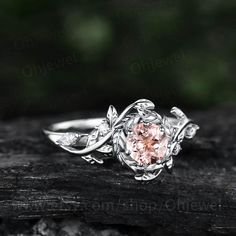 a pink diamond ring sitting on top of a piece of wood with leaves around it