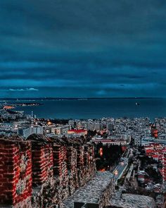 an aerial view of a city at night with the ocean in the background and dark clouds overhead