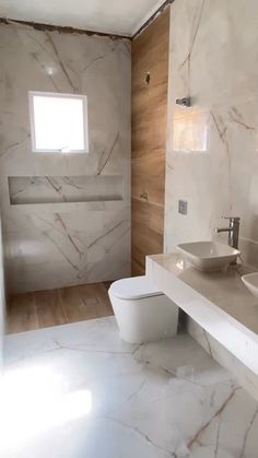 a white bathroom with two sinks and a toilet in it's center wall, next to a window