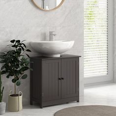 a white sink sitting on top of a wooden cabinet next to a potted plant