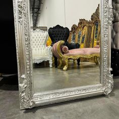 a large silver framed mirror sitting on top of a floor next to a white chair