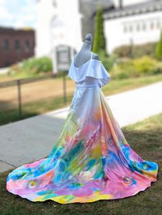 a colorful dress is on display in the grass near a sidewalk and building behind it