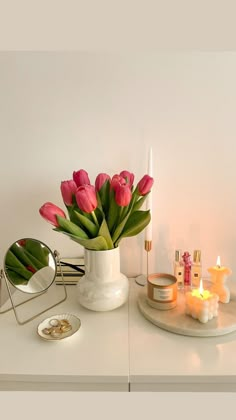 a white vase filled with pink tulips on top of a table next to candles