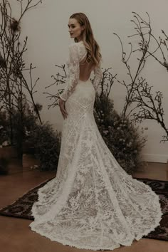 a woman in a white wedding dress standing next to some branches and flowers with her back turned