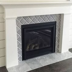 a white fireplace with a black mantle and tile on the wall behind it, in a living room