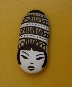 a painted rock with a woman's face on it, against a yellow background