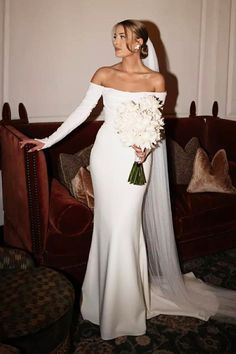 a woman in a white wedding dress standing next to a couch with flowers on it