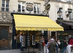 people are walking around in front of a store on the street with yellow awnings