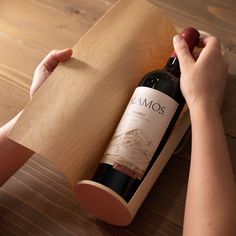 a person opening a bottle of wine in a box on a wooden table with a piece of paper next to it