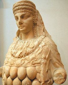 a statue of a woman holding grapes in her hands and wearing a headdress