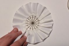 a hand holding a white paper fan on top of a table