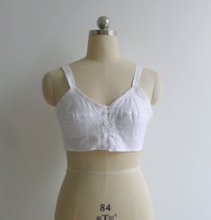 "Brand new vintage deadstock from the 1970's. Soviet era white longline bra top in 100% cotton. Features darted bra cups with circle stitching to the bottom half, slim shoulder straps & a sweet picot trim to the bustline. Closes with a column of buttons to the center front. Could be worn as an undergarment, or even as a cropped camisole top. 100% cotton takes dye well & could be a fun project too! Check out other brassieres in the shop - www.etsy.com/shop/fivestonesvintage?section_id=100 Fitted Cotton Crop Top With Built-in Bra, Fitted Cotton Camisole For Daywear, White Tops With Built-in Bra And Underbust Shape, White Fitted Bra With Spaghetti Straps, Fitted Bra-friendly Tops For Daywear, Fitted White Camisole With Removable Bra Pads, Fitted Cotton Bra With Medium Bust Support, Vintage Cotton Cami Top, Summer Vintage Top With Built-in Bra