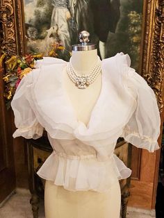 Original Price 145.00 A beautiful vintage off white sheer organza evening blouse adorned with 3-tier ruffled large collars and puff sleeves. There are 3 tiers of organza layers on the beautiful collar which is edged with a thin line of ecru trim. The flounce, sleeves and waist also has the trim. The sleeves are gorgeous as they are large and puffy. The blouse had a hook and eye in front but the hook part needs to be replaced as it has been twisted and not workable. (Easy fix) (Last photo).  The eye part is on the blouse  is fine.  The elastic needs to be replaced in the sleeves and the waist and the cleaners can easily do that or the next owner can.  Both of these are easy fixes. Perfect with an evening skirt, slacks or jeans for this summer.  You just do not see blouses as pretty or elega 70s Blouse, Evening Blouses, Evening Skirts, Ruffled Collar, Blouse Vintage, Character Outfits, Sheer Blouse, Favorite Things Gift, Puff Sleeves