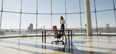 a woman is sitting at a desk in an office setting with large windows overlooking the city