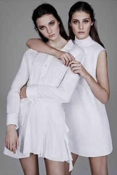 two women standing next to each other in white dresses