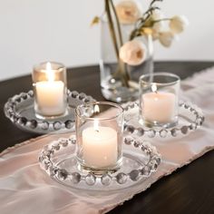 three candles are sitting on a glass plate with beaded trim around the edge, and one candle is lit