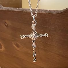 a silver cross is hanging from a chain on a wooden surface with wood planks in the background