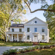 a large white house sitting on top of a lush green field in front of trees