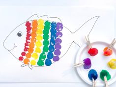 a paper plate with paint and rainbow fish on it next to some crayons