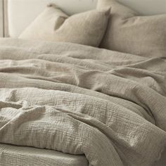 an unmade bed with beige linens and pillows