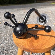 a metal sculpture sitting on top of a wooden table next to a gravel road with trees in the background