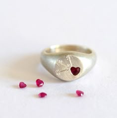 The Ruby Heart Signet Ring, with it's hand engraved Cupid arrows, is designed to be a totally romantic silver signet ring.  Initially carved in jewellers wax, the ring is carefully cast in Sterling Silver so that it is solid, strong and has a super tactile and substantial weight to it. The Ruby is a fully faceted heart which sparkles and changes shades of red in the light, this looks fab with the gentle matt finish of the ring and it's cupid arrows. The ring would also be super awesome in gold, Signet Ring Design Ideas, Hand Made Silver Ring, Heart And Hand, Heart Signet Ring, Silver Ruby Ring, Jewelry Wax, Wax Ring, Diamond Signet Ring, Ruby Heart