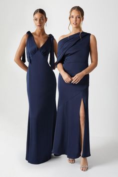 two women in long dresses standing next to each other wearing one shoulder dress and the other with an asymmetrical neckline