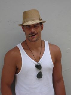 a man wearing a white tank top and a straw hat is standing in front of a wall